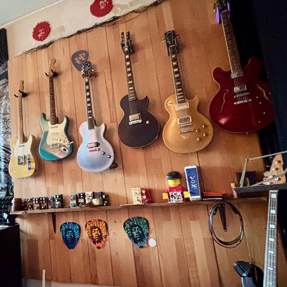 Mattis Gitarrenwand: sechs E-Gitarren an einer Holzwand, darunter ein Regal mit Effektpedalen